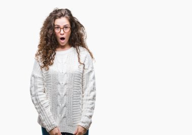 Güzel esmer kıvırcık saçlı Genç kız korkuyor ve şok sürpriz ifade, korku ve heyecan yüz ile izole arka plan üzerinde kış kazak giyiyor.