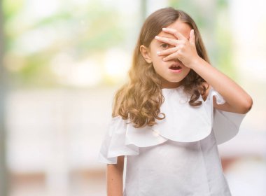 Mahcup ifadeyle parmaklarımın arasından seyir esmer İspanyol kız yüz ve gözler el ile kapsayan şok bakmak.