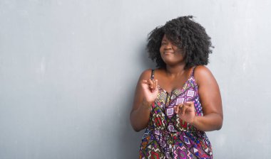 Renkli elbise gri grunge duvarın üzerinden genç Afro-Amerikan kadın tiksinti ifadesi, memnun ve korkulu tiksinti yüz yapıyorsun çünkü nefret tepki. Elleriyle kaldırdı. Sinir bozucu kavramı.