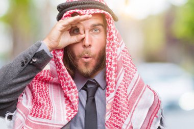 Sürpriz yüz, göz parmaklarının arasından seyir ile uzun saçlı keffiyeh ok jest yapıyor izole arka plan üzerinde giyen genç yakışıklı Arap adam şok. İmansız ifade.