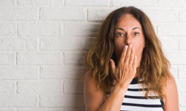 Sessizlik, gizli kavramı orta yaş İspanyol kadın beyaz tuğla duvar kapağı ağız elle hata, korku, ifade için utanç ile şok yüzünden korkuyor