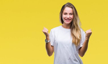 İzole arka plan kutlama üzerinde rahat beyaz t-shirt giyen genç güzel sarışın kadın şaşırttı ve silah ile başarı için yükseltilmiş ve açık gözler hayrete düşürdü. Kazanan kavramı.