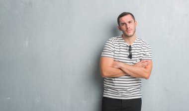 Gri grunge duvar şüpheci ve sinir, onaylamayan ifade yüz çapraz kolları olan genç beyaz adam. Negatif kişi.