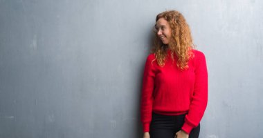Gri grunge genç Kızıl saçlı kadın duvar giyen kırmızı kazaklı uzak tarafına gülümseme ile yüzünde, doğal ifade arıyorum. Kendine güvenen gülüyor.