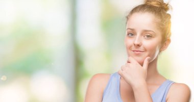 Sarışın genç kadın emin çapraz kollar ve çeneme kaldırdı el ile gülümseme ile kameraya bakıyor. Pozitif düşünce.