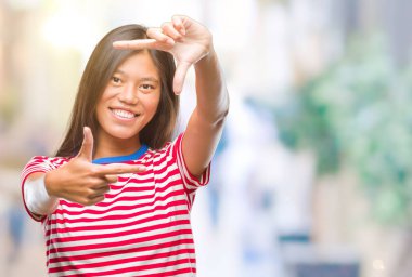 Genç Asyalı kadın elle yapma çerçeve ve parmakları ile mutlu yüz gülümseyen izole arka plan üzerinde. Yaratıcılık ve Fotoğrafçılık kavramı.