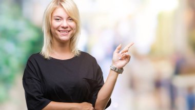 Yüzünde kocaman bir gülümseme ile izole arka plan üzerinde genç güzel sarışın kadın kameraya bakarak yan el ve parmak ile işaret.