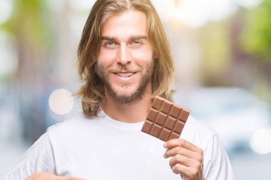 Sürpriz ile izole arka plan üzerinde çikolata yeme uzun saçlı yakışıklı delikanlı yüz kendine işaret parmağı