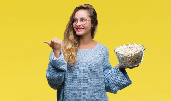 Genç güzel sarışın kadın işaret ve başparmak kadar mutlu yüz gülümseyen tarafı ile gösteren izole arka plan üzerinde patlamış mısır yemek