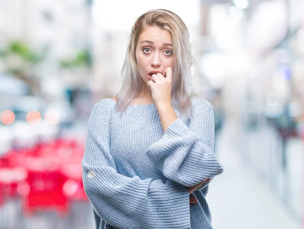 Stresli ve gergin elle çivi ısırma ağzına bakarak izole arka plan üzerinde kış kazak giyen genç sarışın kadın. Anksiyete sorunu.