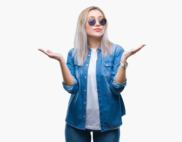 年轻的金发女人戴着太阳镜在孤立的背景下无能和混淆的表达与手臂和手提出 怀疑概念 — 图库照片