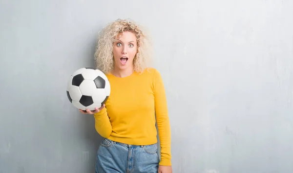Junge Blonde Frau Mit Grunge Grauem Hintergrund Hält Fußballball Erschrocken — Stockfoto