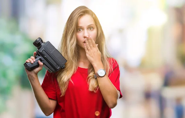 Young beautiful blonde woman filming using vintage camera over isolated background cover mouth with hand shocked with shame for mistake, expression of fear, scared in silence, secret concept