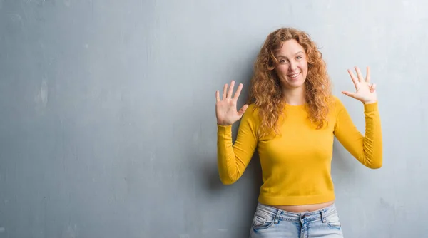 灰色のグランジの壁を示すと指で上向きに若い赤毛の女性ナンバー ナイン自信を持って 幸せな笑みを浮かべて — ストック写真