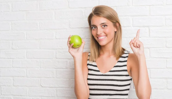 Hermosa Mujer Joven Sobre Pared Ladrillo Blanco Comiendo Manzana Verde —  Fotos de Stock