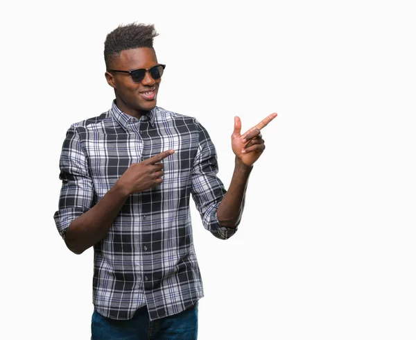 年轻的非洲裔美国男子戴着太阳镜在孤立的背景下微笑着 看着相机指着两个手和手指的侧面 — 图库照片