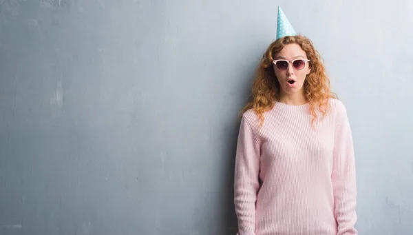 Joven Pelirroja Sobre Pared Grunge Gris Usando Gorra Cumpleaños Asustada — Foto de Stock