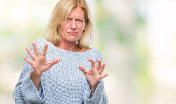 Middle age blonde woman wearing winter sweater over isolated background disgusted expression, displeased and fearful doing disgust face because aversion reaction. With hands raised. Annoying concept.