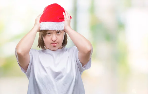 Young adult woman with down syndrome wearing christmas hat over isolated background suffering from headache desperate and stressed because pain and migraine. Hands on head.