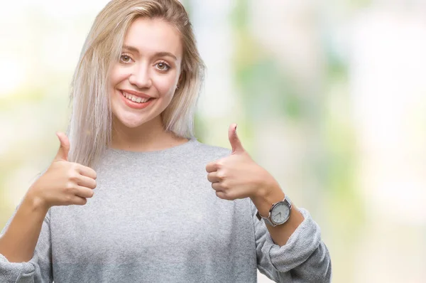Young blonde woman over isolated background success sign doing positive gesture with hand, thumbs up smiling and happy. Looking at the camera with cheerful expression, winner gesture.