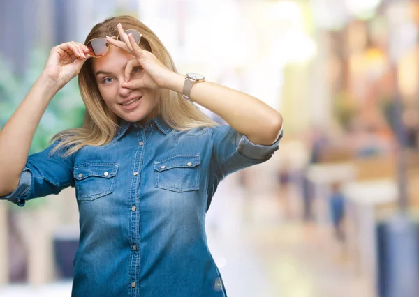 幸せそうな顔で指を通して見る目の手で のジェスチャーを行う分離の背景の上にサングラスをかけている若い白人女性 — ストック写真