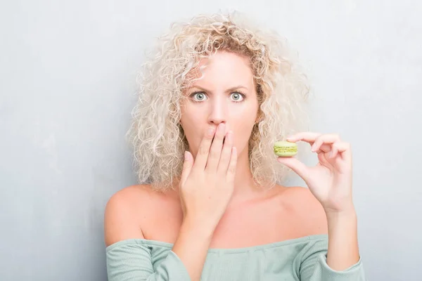 Joven Rubia Sobre Fondo Gris Grunge Comiendo Macaron Cubrir Boca —  Fotos de Stock