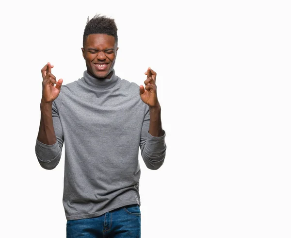 在孤立的背景下 年轻的非洲裔男子微笑着交叉手指与希望和眼睛闭上 运气和迷信概念 — 图库照片