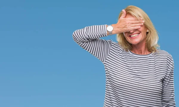 Middle age blonde woman over isolated background smiling and laughing with hand on face covering eyes for surprise. Blind concept.