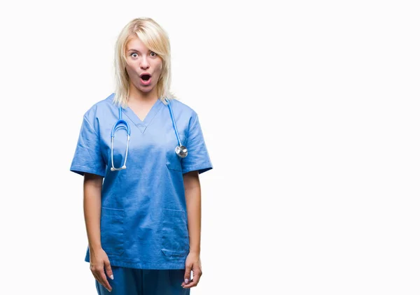 驚きの表情でショックを受けて孤立の背景に美しい金髪女医女性身に着けている医療制服恐怖し 興奮の顔 — ストック写真