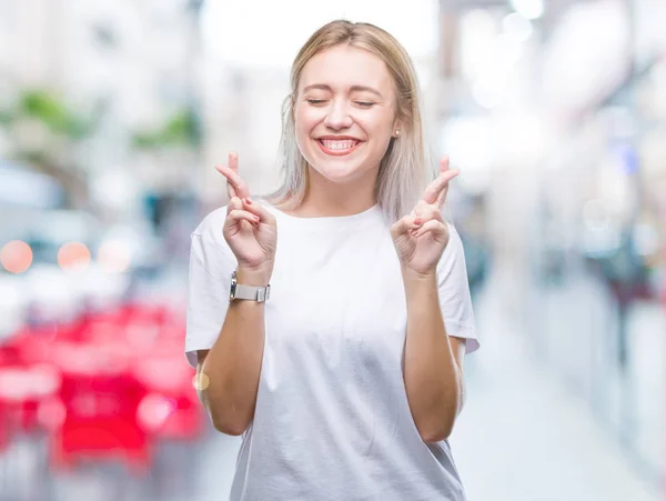 年轻的金发女人在孤立的背景下微笑着交叉手指 希望和眼睛闭上 运气和迷信概念 — 图库照片