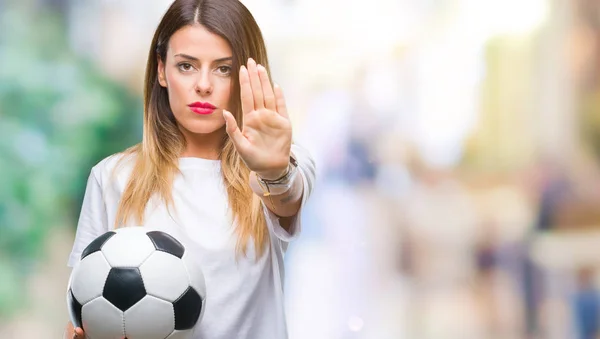 Young beautiful woman holding soccer ball over isolated background with open hand doing stop sign with serious and confident expression, defense gesture