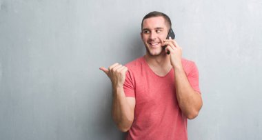 İşaret ve başparmak kadar mutlu yüz gülümseyen tarafı ile gösterilen telefonda konuşurken gri grunge duvarın üzerinden beyaz delikanlı