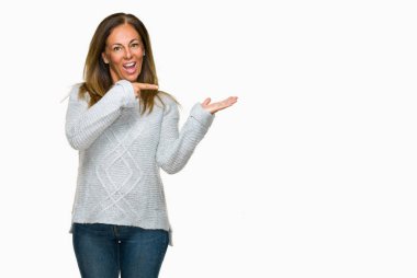 Hayret ve el ile sunulması ve parmak ile işaret ederken kameraya gülümseyen izole arka plan üzerinde kış kazak giyen güzel orta yaş yetişkin kadın.