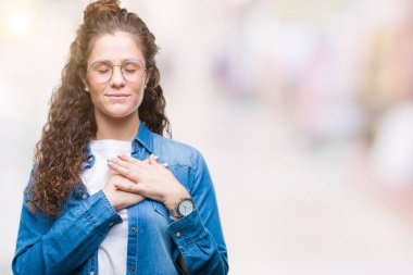 Güzel genç esmer kıvırcık saçlı kız göğüs kapalı gözlerle ellerinde ve yüzünde minnettar jest ile gülümseyen izole arka plan üzerinde gözlük takıyorum. Sağlık kavramı.