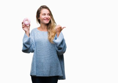 Genç güzel sarışın kadın işaret ve başparmak kadar mutlu yüz gülümseyen tarafı ile gösteren izole arka plan üzerinde tatlı çörek yeme