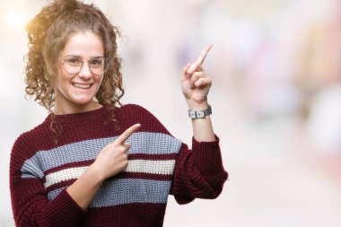 Güzel esmer kıvırcık saçlı Genç kız gülümseyerek ve iki elleri ve parmakları ile tarafına işaret kamera bakarak izole arka plan üzerinde gözlük.