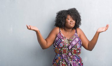 Gri grunge duvar renkli elbise clueless ve şaşkın bir ifadeyle kollar ve eller kaldırdı giyen genç Afro-Amerikan kadın. Şüphe kavramı.