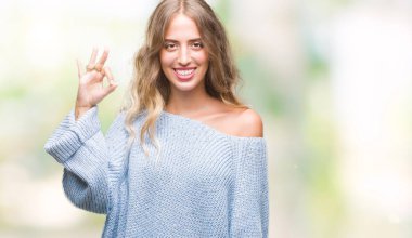 İzole arka plan el ve parmaklar ok işaretiyle yapıyor olumlu gülümseyen üzerinde kış kazak giyen güzel genç sarışın kadın. Başarılı ifade.