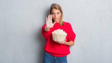 Grunge gri duvar açık eliyle dur işareti ile ciddi ve kendine güvenen ifade, savunma jest yapıyor pop mısır yemek güzel genç kadın