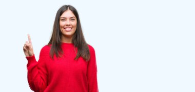 Genç güzel İspanyol giyen kırmızı kazaklı gösterme ve kendinden emin ve mutlu gülümseyen bir parmak ile işaret eden oktan yukarı.