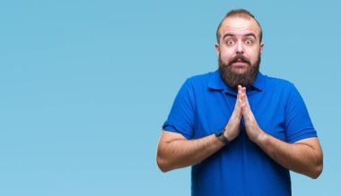 Ellerle birlikte AF emin gülümseyen için soran dua izole arka plan üzerinde mavi gömlek giymiş genç beyaz hipster adam.