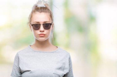 Sarışın genç kadın yüzünde ciddi bir ifade ile izole arka plan üzerinde güneş gözlüğü takıyor. Basit ve doğal kameraya bakıyor.