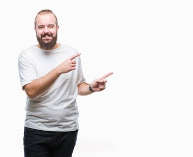 Gülümseyen ve iki elleri ve parmakları ile tarafına işaret kamera bakarak izole arka plan üzerinde rahat t-shirt giyen genç beyaz hipster adam.