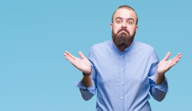 Genç beyaz hipster adam izole arka plan clueless ve şaşkın bir ifadeyle kollar ve eller kaldırdı. Şüphe kavramı.