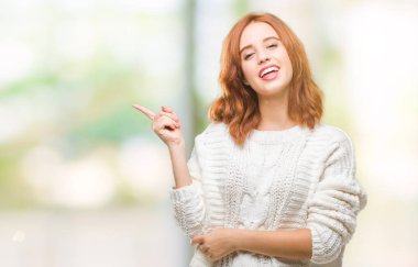 Kameraya bakarak yan el ve parmak ile işaret izole arka yüzünde, kocaman bir gülümseme ile kış kazak giyen genç güzel kadın.