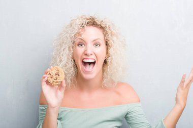 Sarışın genç kadın grunge üzerinde gri duvar büyük gülümseme ile çığlık ve ellerini kaldırdı kazanan ifade kutluyor zafer çikolatalı bisküvi çok mutlu ve heyecanlı, yemek