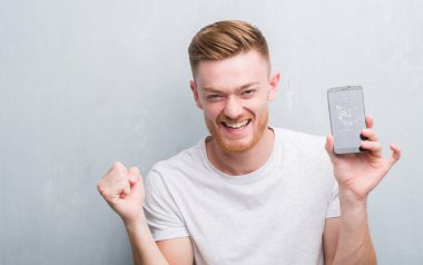 Duygu tezahürat genç Kızıl saçlı adam gurur çığlık ve zafer ve başarı çok heyecanlı, kutluyor kırık smartphone tutan gri grunge duvarın üzerinden