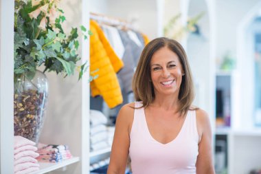 Güzel orta yaş İspanyol kadın giyim mağazasında yüzünde gülümseme ile ayakta. Dükkan sahibi ve tezgâhtar kendinden emin ve neşeli gülümseyen