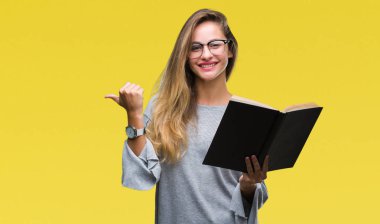 Genç güzel sarışın kadın işaret ve başparmak kadar mutlu yüz gülümseyen tarafı ile gösteren izole arka plan üzerine bir kitap okuma