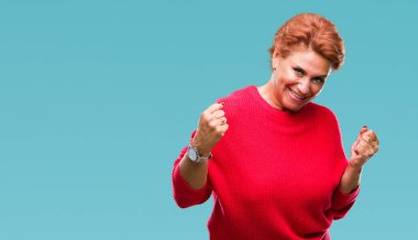 Üzerinde kış kazak giyen Atrractive üst düzey beyaz Kızıl saçlı kadın gülümseyerek ve başarı için çığlık arka plan çok mutlu ve heyecanlı kaldırdı, silah ile kazanan jest yapıyor izole. Kutlama kavramı.